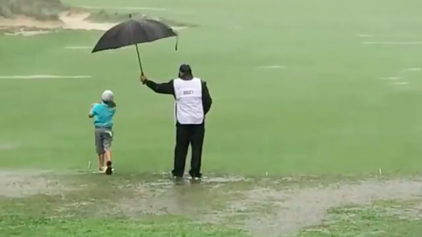 WATCH: Caddie protects young golfer from TORRENTIAL weather conditions